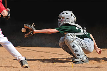 Catcher bent down about to catch a pitched ball.