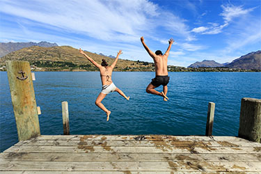 Man and women jumping off the dock into lake.