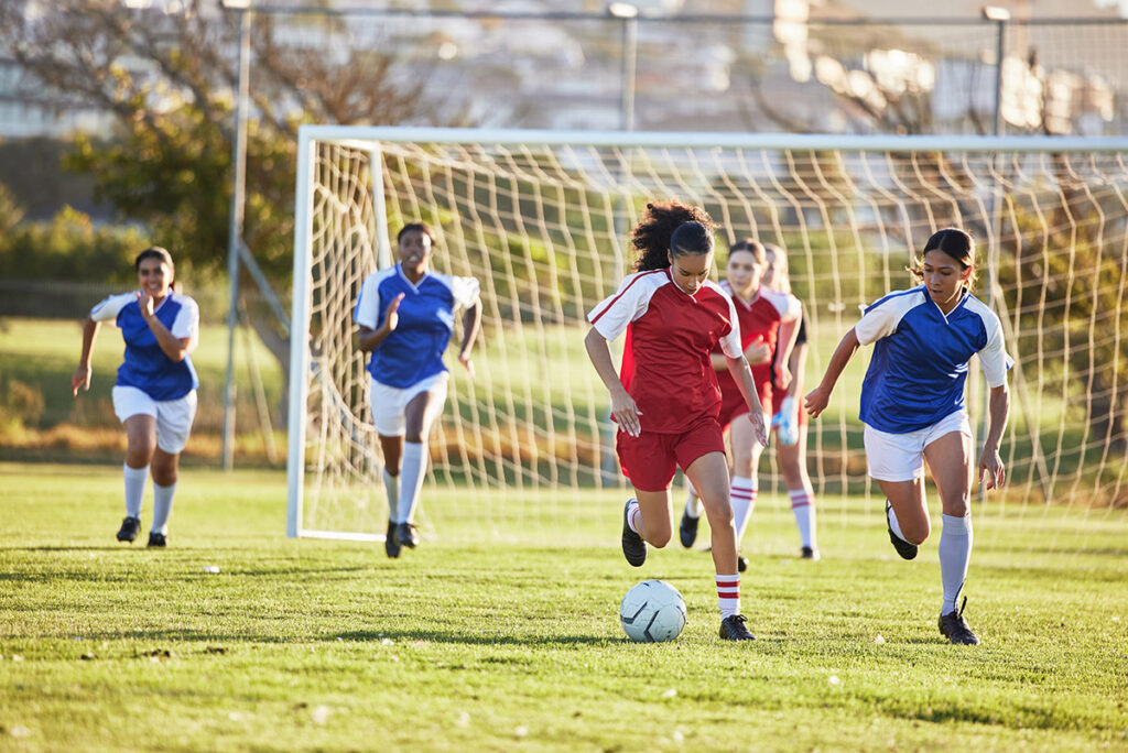 A woman's sports team kicking a ball down the field.